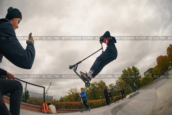 Moscow, Russia - August 27, 2019: Teenager performs a trick on sportive push scooter on a city sports ground. He jumping. Extreme sports is very popular. Редакционное фото, фотограф YuryKara / Фотобанк Лори