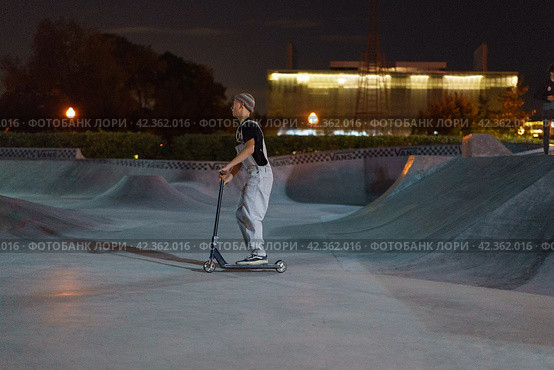 Moscow, Russia - August 27, 2019 Teenager ready to perform a trick at sportive push scooter on a city sports ground. He jumping over an obstacles. Extreme sports is very popular among youth. Side view. Редакционное фото, фотограф YuryKara / Фотобанк Лори
