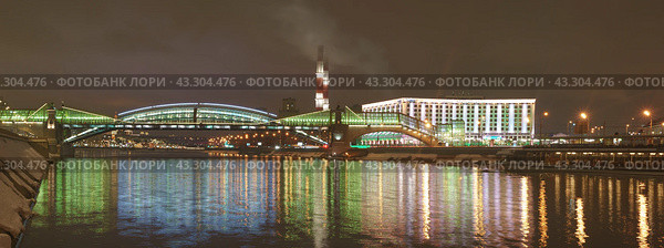 Moscow, Russia - February 6, 2019: New Pedestrian Bridge of Bogdan Khmelnitsky near the Kievsky railway Station and Radisson Slavyanskaya Hotel. Bright spring night in city lights. Panoramic image. Редакционное фото, фотограф YuryKara / Фотобанк Лори