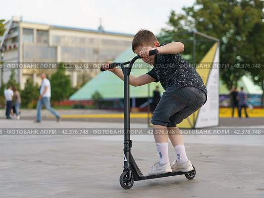 Moscow, Russia - July 26, 2019 Teenager ready to perform a trick at sportive push scooter on a city street. Редакционное фото, фотограф YuryKara / Фотобанк Лори