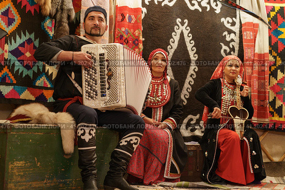 Moscow, Russia - September 15, 2019: Traditional atmosphere, bright home furniture, decoration in Bashkiria. Old lifestyles, fashion at home. Floral pattern of carpet. Family play squeezebox and kubyz. Редакционное фото, фотограф YuryKara / Фотобанк Лори