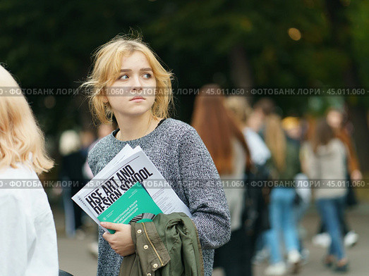 Moscow, Russia - September 5, 2019: Portrait of young woman with a newspaper visiting the city festival in the Gorky park. A crowd of youth around her. Blurred background. Редакционное фото, фотограф YuryKara / Фотобанк Лори