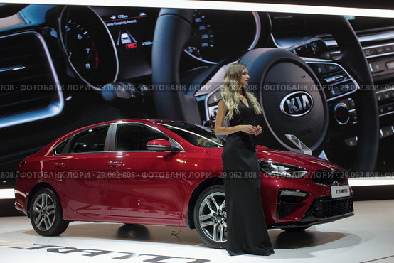 Московский автосалон 2018 года, девушка модель у красного автомобиля KIA на фоне большого руля. Редакционное фото, фотограф Дмитрий Неумоин / Фотобанк Лори