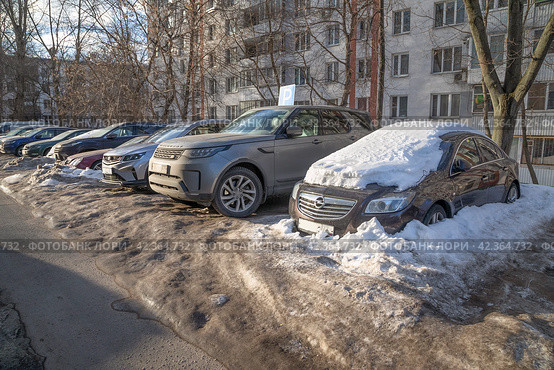 Москва, март. Вросшие в снег и лед машины, стоящие на парковке во дворе многоквартирного дома (2024 год). Редакционное фото, фотограф Наталья Николаева / Фотобанк Лори