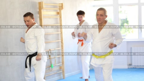 Motivated sporty elderly man wearing white kimono with yellow belt performing kata routines to hone martial arts skills in training room with group of fighters. Стоковое видео, видеограф Яков Филимонов / Фотобанк Лори