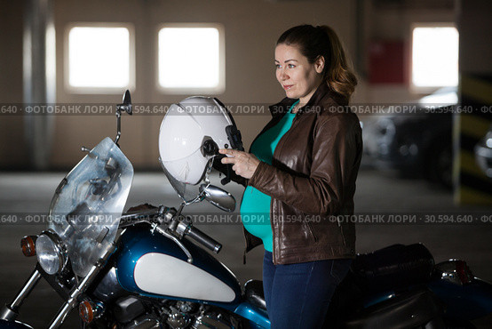 Motorcyclist pregnant woman preparing to ride chopper bike, put on her helmet at parking lot. Стоковое фото, фотограф Кекяляйнен Андрей / Фотобанк Лори