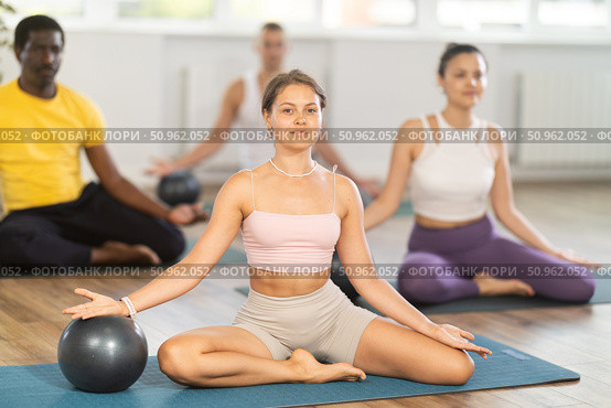 Multinational athletes sitting on floor in asana pigeon do body tilts to side, use fitball. Стоковое фото, фотограф Яков Филимонов / Фотобанк Лори