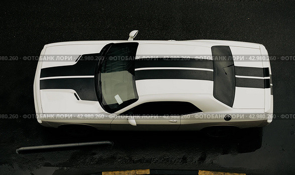 Muscle car Dodge Challenger SRT parked on wet asphalt road, top view. Aerial photo of white auto with black stripes. Редакционное фото, фотограф Константин Григорьев / Фотобанк Лори