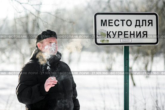 Мужчина курит сигарету возле таблички "Место для курения" морозным днём. Стоковое фото, фотограф Игорь Низов / Фотобанк Лори