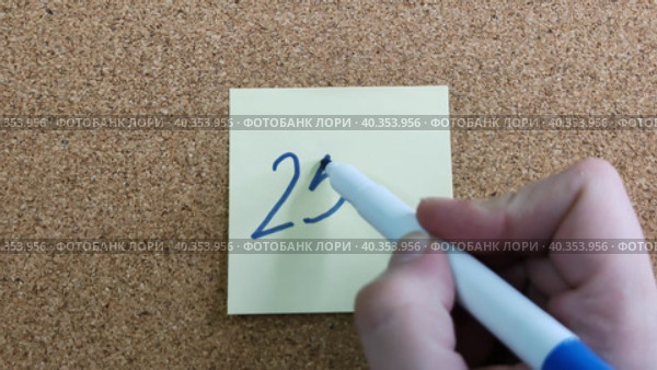 Надпись 25% на бумажном стикере приклеенном к пробковой  доске. Женщина пишет маркером на желтой бумаге. Синий фломастер в женской руке. Рукописный текст красивым почерком. Процент скидки или прибыли. The inscription is 25% on a paper sticker glued to a cork board. A woman writes with a marker on yellow paper. A blue felt-tip pen in a woman's hand. Handwritten text in a beautiful handwriting. Percentage of discount or profit. Стоковое видео, видеограф Ирина / Фотобанк Лори