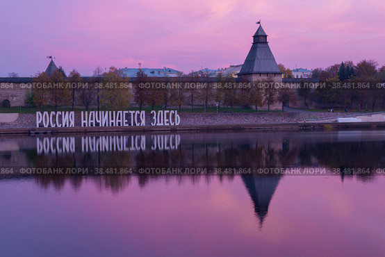 Надпись-инсталяция "Россия начинается здесь" на фоне Псковского кремля в октябрьским сумерки (2018 год). Редакционное фото, фотограф Виктор Карасев / Фотобанк Лори
