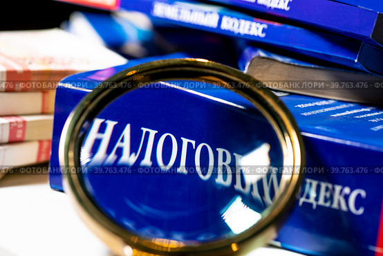 Налоговый кодекс под увеличительным стеклом лежат на столе (2023 год). Редакционное фото, фотограф Николай Винокуров / Фотобанк Лори