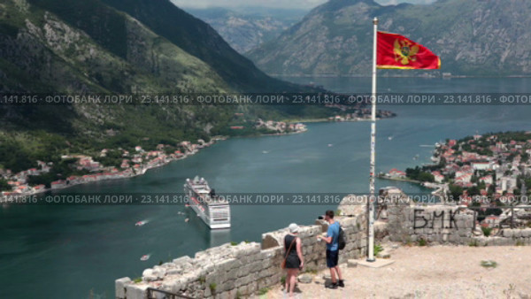 Национальный флаг Черногориии над крепостью St. John на фоне Которской бухты. Туристы на обзорной площадке. Котор, Черногория (2016 год). Стоковое видео, видеограф Кекяляйнен Андрей / Фотобанк Лори