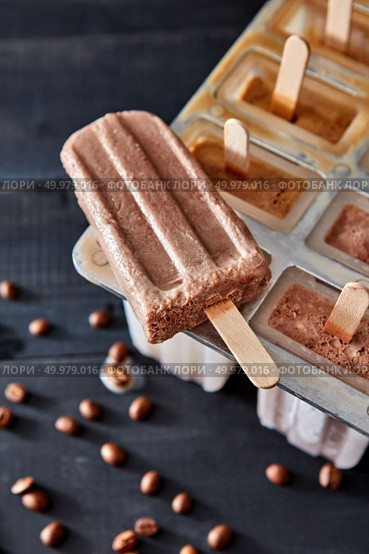 Natural coffee ice cream popsicle with coffee beans presented on a black wooden table. Summer dessert. Top view. Sweet homemade coffee ice lolly on a dark wooden table with coffee beans. Top view. Стоковое фото, агентство Ingram Publishing / Фотобанк Лори