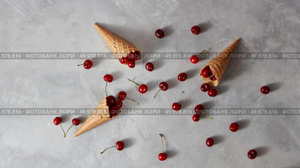 Natural freshly picked fruits cherries for homemade cookies, cakes and waffle cones on a gray background with place for text. Organic vegetarian raw eating.. Pattern of freshly picked ripe cherries in a sweet wafer cones on a gray concrete table. Cherry on a table. Стоковое фото, агентство Ingram Publishing / Фотобанк Лори