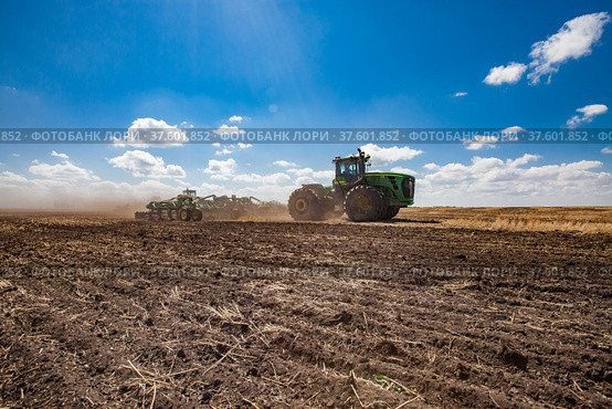 North Kazakhstan Province, Kazakhstan-May 12, 2012: Spring sowing campaign. John Deere tractors cultivating soil with harrow. Blue sky, clouds. Редакционное фото, фотограф Alexey Rezvykh / Фотобанк Лори