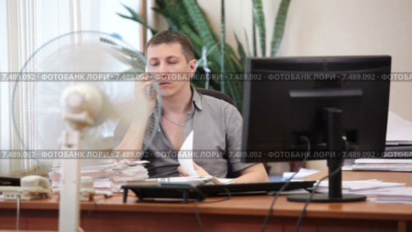 Офисный служащий звонит по сотовому телефону на рабочем месте с включенным охлаждающим вентилятором. Стоковое видео, видеограф Кекяляйнен Андрей / Фотобанк Лори