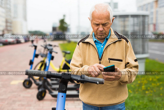 Old man using smartphone to activate e-scooter. Стоковое фото, фотограф Татьяна Яцевич / Фотобанк Лори