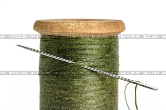 Old Single wooden spool of thread olive green color and needle closeup white background. Стоковое фото, фотограф Camptoloma / Фотобанк Лори