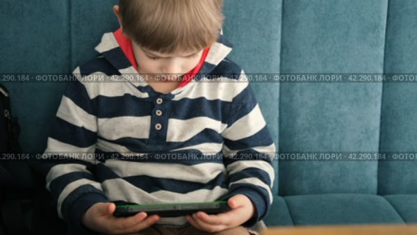 One toddler boy using smartphone sitting in cafe, restaurant. Child looking at mobile phone, modern parenting concept. Lifestyle with digital gadget devices. Bored kid relax with play game on a cell. Стоковое видео, видеограф Марина Демидюк / Фотобанк Лори