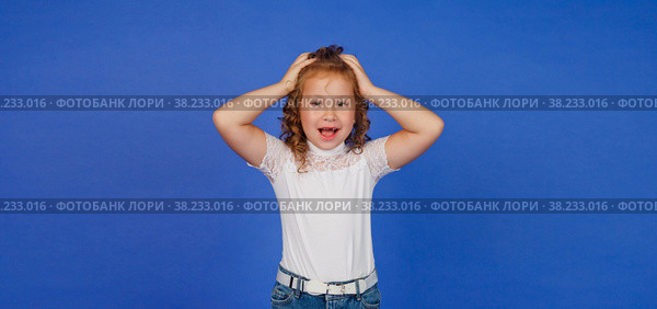 Oops concept or emotion of winner. Shocked girl clutches head, opens toothless mouth, stunned by news, on blue background. Unsuccessful examination results and certification of education. Copy space. Стоковое фото, фотограф Aleksandr Golubev / Фотобанк Лори