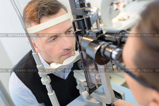 optometrist in exam room with man in chair. Стоковое фото, агентство Ingram Publishing / Фотобанк Лори