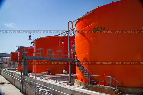 Orange metal storage tanks with acid and its formula on sulfuric (sulphuric) acid plant warehouse. Clear blue sky. Стоковое фото, фотограф Alexey Rezvykh / Фотобанк Лори