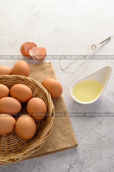 Organic eggs on sack cloth, many eggs on wicker basket and glasses bowl, oil and egg whisk placed on the floor, preparing for cooking food or dessert, copy space. Стоковое фото, агентство Ingram Publishing / Фотобанк Лори