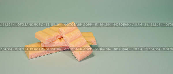 Пачка батончиков молочного шоколада со вкусом клубники с игристой текстурой на пастельном мятно-зеленом фоне, символизирующая концепцию сладких десертов, кондитерских изделий и закусок. copy space. Стоковое фото, фотограф Анна Чижова / Фотобанк Лори