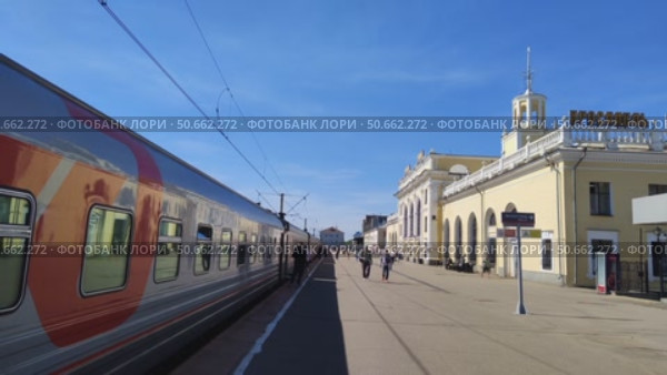 Пассажирский поезд стоит на перроне у старинного здания железнодорожного вокзала. Люди ходят по перрону вдоль вагонов.  Россия, Ярославль, 22 мая 2025. Редакционное видео, видеограф Ирина / Фотобанк Лори