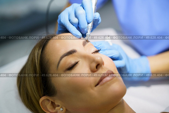 Permanent make-up for eyebrows of beautiful woman in a beauty salon. Close-up of beautician doing tattooing eyebrow. Micropigmentation treatment.. Permanent make-up for eyebrows of beautiful woman in a beauty salon. Micropigmentation treatment. Стоковое фото, агентство Ingram Publishing / Фотобанк Лори