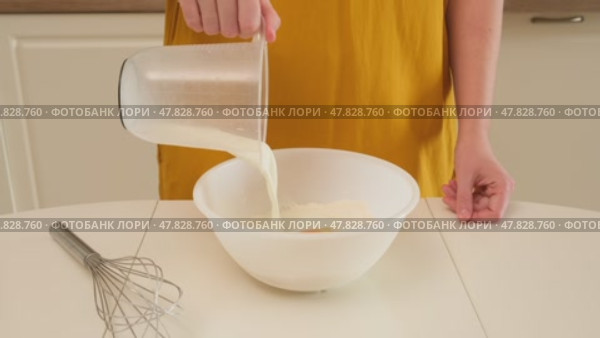 Person pouring milk from measuring jug into bowl with flour. Studio kitchen scene. Dough making process and baking ingredient concept. Close-up shot. Стоковое видео, видеограф Андрей Журавлев / Фотобанк Лори
