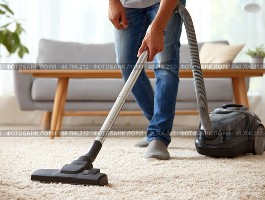 Person using vacuum cleaner on carpeted floor in a bright living room with modern furniture. Стоковое AI-изображение, AI-художник Гайфуллина Дина / Фотобанк Лори