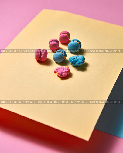 Pink bright macaroons are presented in the form of a triangular pyramid on yellow cardboard and one crushed macaroon on a pink paper background with reflection of shadows. Creative composition. Original composition of colorful macaroons on a yellow paper on paper background. Стоковое фото, агентство Ingram Publishing / Фотобанк Лори