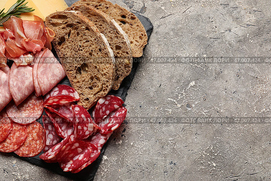 Плита из сланца с ассортиментом вкусных деликатесов и хлебом на сером фоне, крупным планом. Стоковое фото, фотограф Pixel_shot / Фотобанк Лори