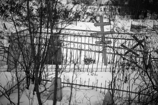 Покосившиеся кресты и заборы в снегу на старом кладбище. Черно-белая фотография могил. Мрачное настроение. Холодная зимняя погода. Малая глубина резкости. Сибирь, Крайний Север России. Стоковое фото, фотограф Андрей Степанов / Фотобанк Лори