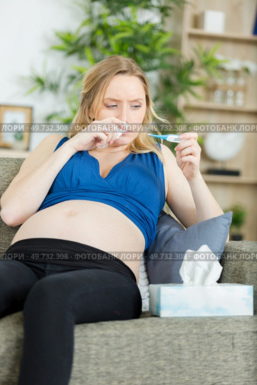 poorly pregnant woman checking her temperature with a thermometer. Стоковое фото, агентство Ingram Publishing / Фотобанк Лори
