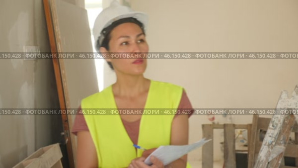 Portrait of a focused woman builder in a hardhat and vest, attentivelly checking the construction panels. Стоковое видео, видеограф Яков Филимонов / Фотобанк Лори