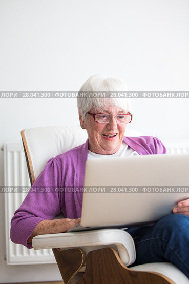 Portrait of a senior woman at home - Laughing at something on her laptop computer, sitting in her favorite chair, enjoying retirement. Стоковое фото, фотограф Viktor Cap / PantherMedia / Фотобанк Лори