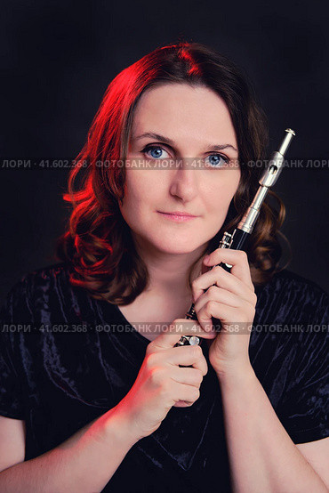Portrait of a woman musician with a piccolo flute on a studio black background. Flutist with a small flute in her hands. Стоковое фото, фотограф Андрей Журавлев / Фотобанк Лори
