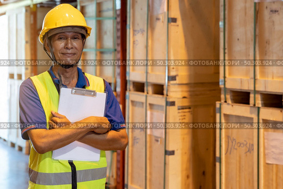 Portrait of Asian warehouse worker with clipboard job cross arm in large distribution warehouse background. Reopening business warehouse inventory and logistic concept. Стоковое фото, агентство Ingram Publishing / Фотобанк Лори