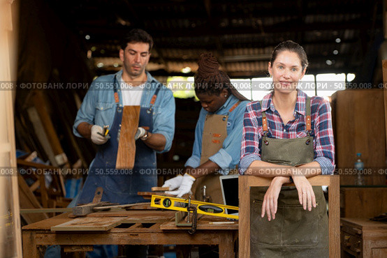 Portrait of carpenter female worker standing in front of colleague in workshop, Eyesight is utilized to ensure accuracy. Стоковое фото, агентство Ingram Publishing / Фотобанк Лори