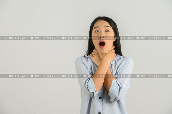 Portrait of Excited young asian woman in blue shirt hand on neck isolated on white background. Expression and lifestyle concept. Стоковое фото, агентство Ingram Publishing / Фотобанк Лори