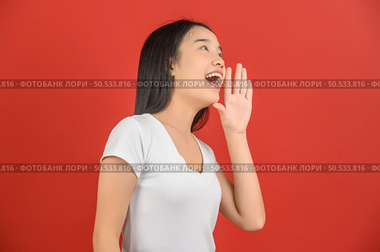 Portrait of Excited young asian woman in white t-shirt shout story or making announcement over isolated white background. Advertising and lifestyle concept. Стоковое фото, агентство Ingram Publishing / Фотобанк Лори