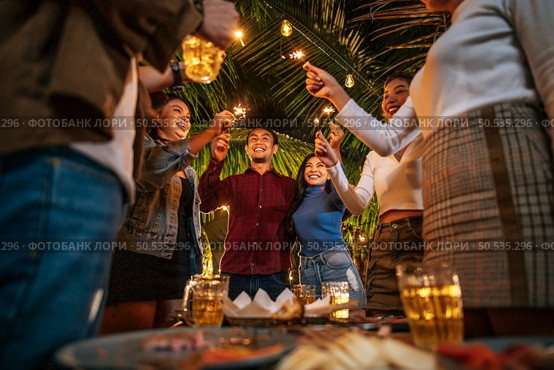 Portrait of Happy Asian group of friends having fun with sparklers outdoor - Young people having fun with fireworks at night time  - People, food, drink lifestyle, new year celebration concept. Стоковое фото, агентство Ingram Publishing / Фотобанк Лори