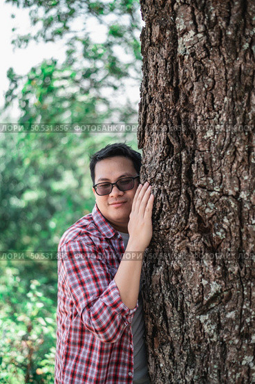 Portrait of Happy Asian man hugging a tree in forest. Protecting and love nature. Environment and ecology concept. Стоковое фото, агентство Ingram Publishing / Фотобанк Лори