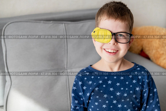 Portrait of little boy wearing glasses with occluder to correct vision sitting on sofa at home. Стоковое фото, фотограф Кашапова Эльвира / Фотобанк Лори