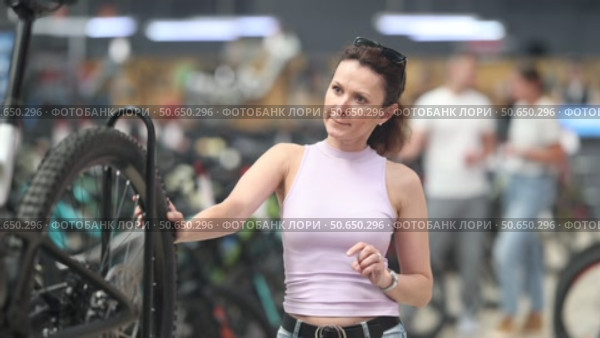 Portrait of positive woman standing in bicycle store and choosing new comfortable bike. Стоковое видео, видеограф Яков Филимонов / Фотобанк Лори