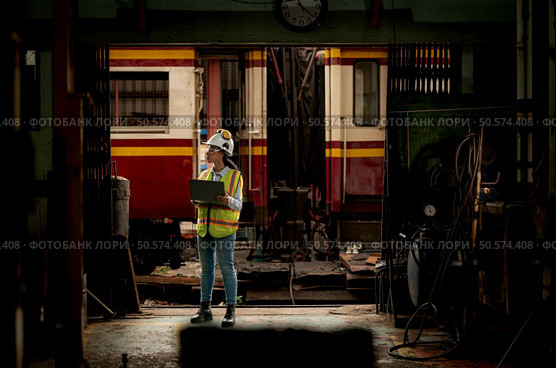 Portrait of railway technician worker in safety vest and helmet working with blueprint at train repair station. Стоковое фото, агентство Ingram Publishing / Фотобанк Лори