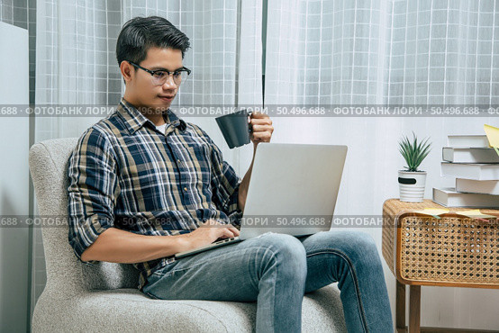 Portrait of smiling handsome man in glasses relaxing with coffee, using technology of laptop computer to working from home during self-isolation and quarantine covid-19 coronavirus outbreak. Стоковое фото, агентство Ingram Publishing / Фотобанк Лори